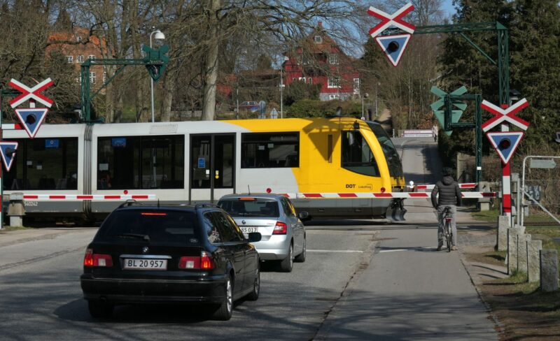 Biler der holde i kø ved jernbaneoverkørsel med krydsende tog.