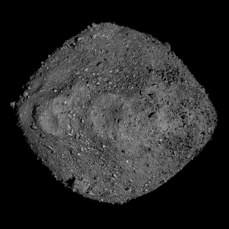 Et gråtonebillede af en klippeagtig, uregelmæssigt formet asteroide med en ru, ujævn overflade dækket af små sten og kampesten, set på en sort baggrund.