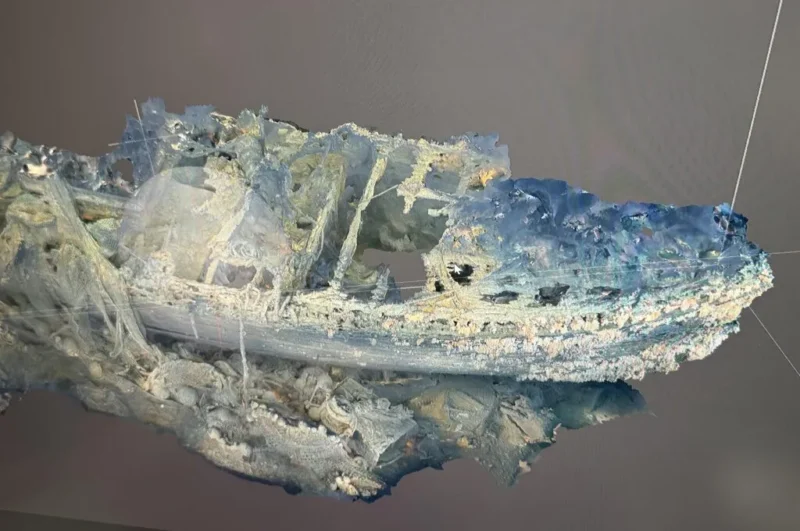 En digital 3D-model af et skibsvrag, vist i nuancer af blåt og hvidt, med synlige skader på skroget og brud på konstruktionen på en ensfarvet grå baggrund.