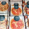Kasser med frosne pizzaer af mærket Solling, herunder salami-, kebab-, bolognese- og specialevarianter, er stablet i en supermarkedsfryser bag et sort metalstativ.