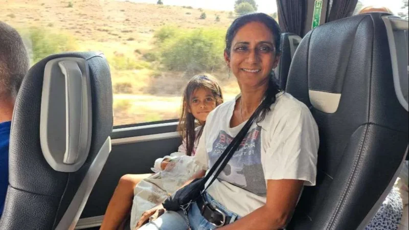 En kvinde og en ung pige sidder sammen i en bus. Kvinden smiler til kameraet; hun har en hvid T-shirt på og solbriller på hovedet. Pigen sidder ved siden af hende i en hvid kjole. Bussen kører gennem et solrigt landskab.