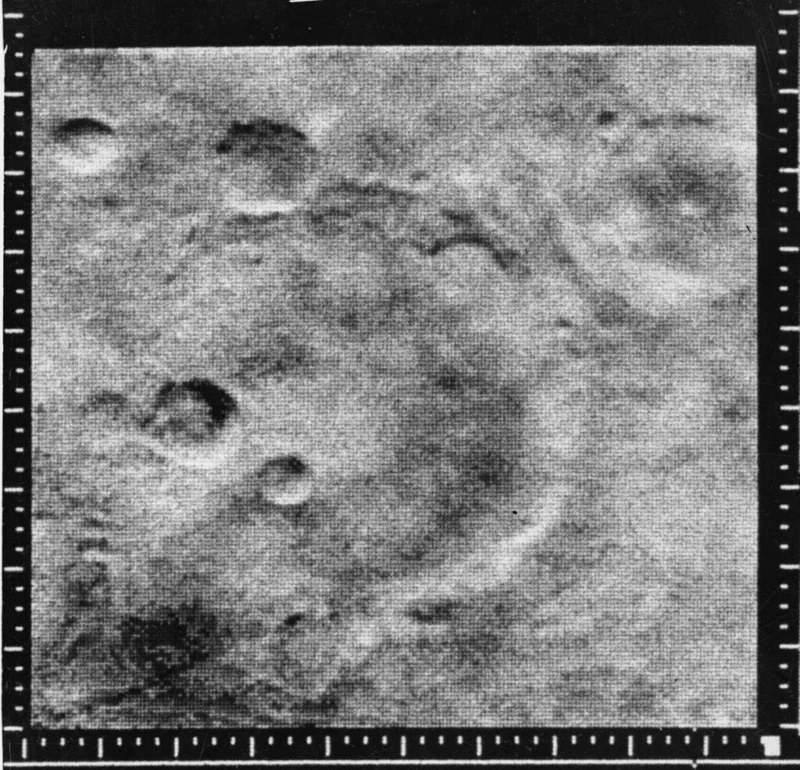 Et sort-hvidt billede viser en kraterfyldt planetoverflade, sandsynligvis Månen eller Mars, med flere cirkulære fordybninger. Hvide målemærker omkranser billedet. Overfladen fremstår ru og stenet.