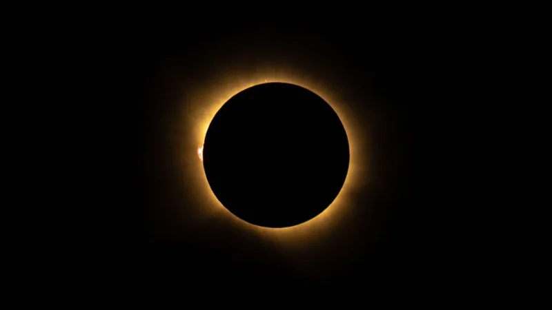 En solformørkelse, hvor Månen helt dækker Solen, hvilket afslører Solens glødende korona og en lys plet, der kaldes »diamantringeffekten«. Himlen omkring er mørk.