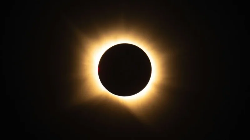 En total solformørkelse, hvor månen fuldstændigt dækker solen, så der kun ses en glødende korona omkring den mørke silhuet mod den sorte himmel.