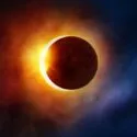 En solformørkelse, hvor månen dækker det meste af solen, så der kun er en lysende ring af lys og farverige skyer i orange, rødt og blåt tilbage omkring månens mørke silhuet.