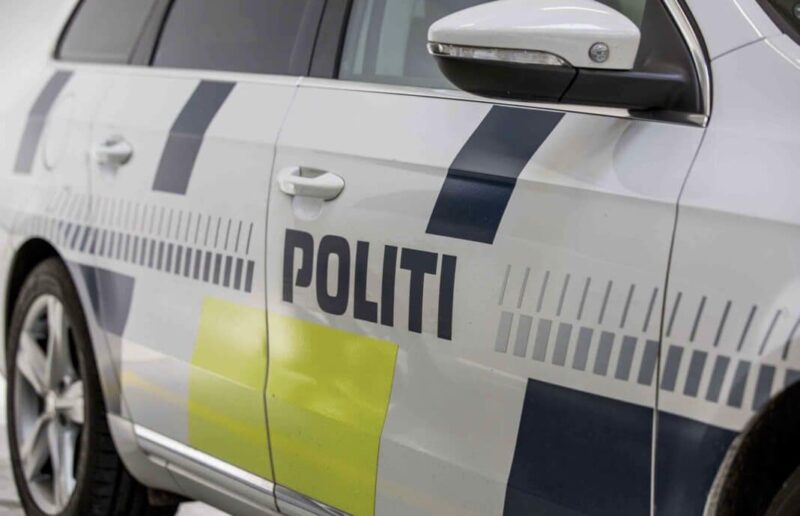 White police car side with reflective blue chevrons and yellow panels, door handle visible