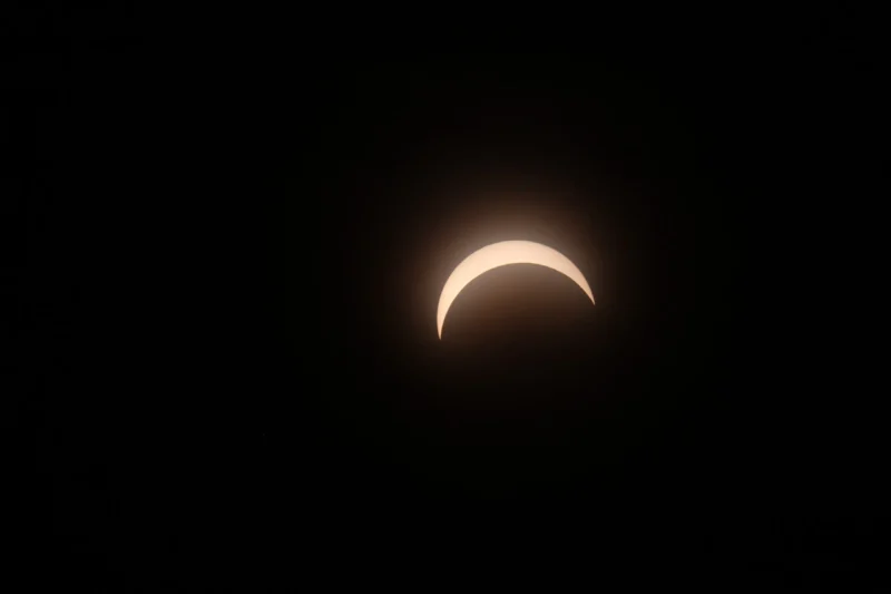 En halvmåneformet solformørkelse viser sig på den mørke himmel, hvor månen delvist dækker solen, og et svagt skær omgiver den oplyste halvmåne.